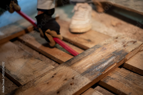 A man’s hands are seen dismantling a wooden pallet using a pry bar. A close-up shot that shows the manual effort involved in salvaging and recycling wood.