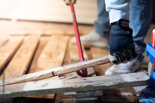 Obraz na płótnie A man is forcefully prying apart a wooden pallet with a crowbar