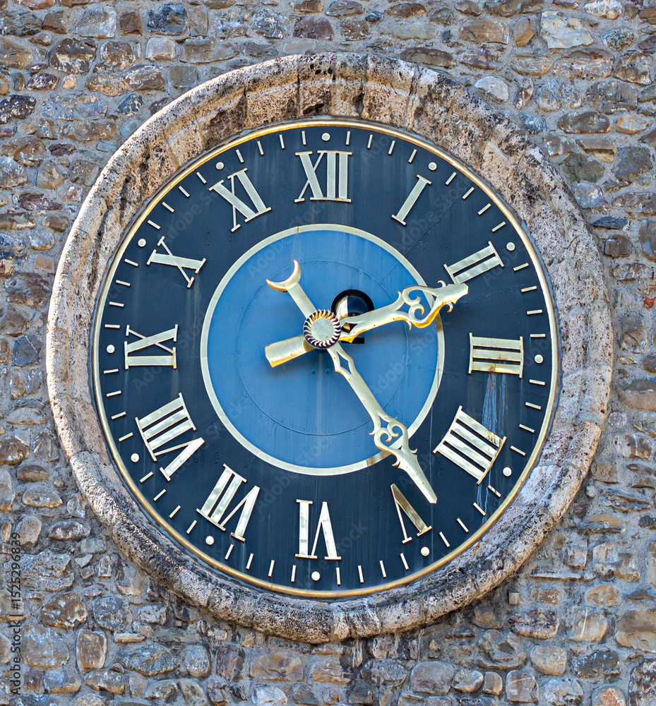 A large stone-framed clock with golden Roman numerals and ornate hands. Set in a rough stone wall, its dark blue face contrasts with the shimmering metal and aged, weathered texture. A large stone-framed clock with golden Roman numerals and ornate hands. Set in a rough stone wall, its dark blue face contrasts with the shimmering metal and aged, weathered texture.