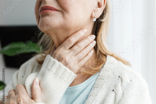 Closeup cropped image of unrecognizable aged female touching her throat being sick, feeling unwell, concerned of her thyroid dysfunction and pain, having endocrine disease of typical flue