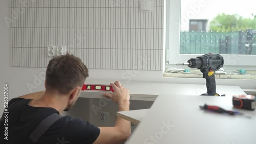 Man uses spirit level to align kitchen countertop panel during installation. Professional kitchen furniture assembly during renovation in new home