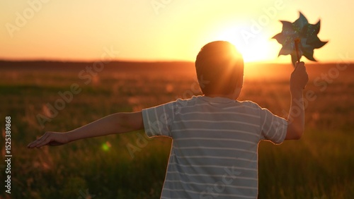 Happy child playing with toy pinwheel outdoors in summer in park against sky. Childhood children. Child boy runs with toy wind pinwheel in his hand on summer field, sun day. Family holiday, nature