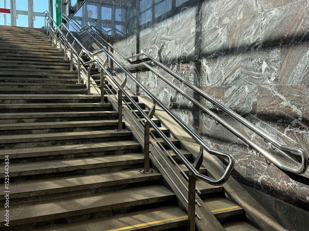 Obraz premium Staircase to an underground passage with a ramp for people with limited mobility. Urban infrastructure concept. Handheld phone photo, selective focus, harsh sunlight, non-AI