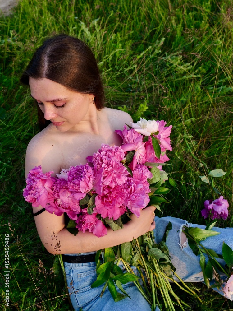 Fototapeta premium Happy smiling young woman in summer outdoors in a field with pink peony flowers enjoying life in a moment at sunset