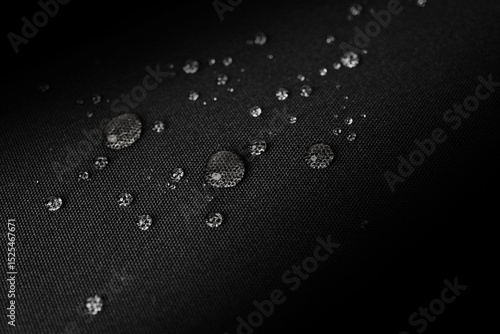 Macro photo of water droplets on black waterproof fabric, showing hydrophobic properties with a clear grid texture under soft lighting, highlighting resistance and surface detail.