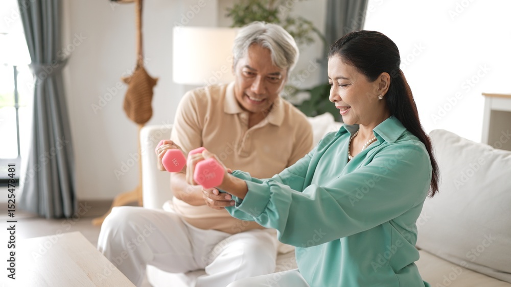 Obraz premium Happy elderly couple exercising together with dumbbells at home, focusing on muscle strength, joint health, and physical wellness for improved mobility and healthy aging. Retirement concept. Myrmidon.