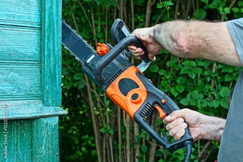 Wallpaper Mural one modern dirty powerful with plastic orange handle electric industrial professional heavy with sharp chain iron black dangerous saw in worker hands cutting wooden green wall of house Torontodigital.ca