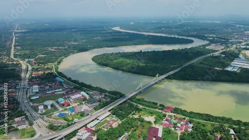 Scenic aerial view of a winding river and long bridge surrounded by green forest and rural town landscape. Beautiful nature and infrastructure.