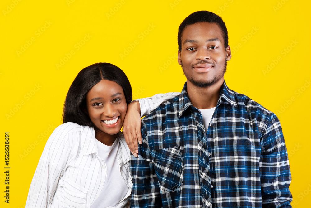 Happy relationship of student and fun together during covid-19 lockdown. Smiling young african american man and woman look at camera, lady put hand on male shoulder, isolated on yellow background Happy relationship of student and fun together during covid-19 lockdown. Smiling young african american man and woman look at camera, lady put hand on male shoulder, isolated on yellow background