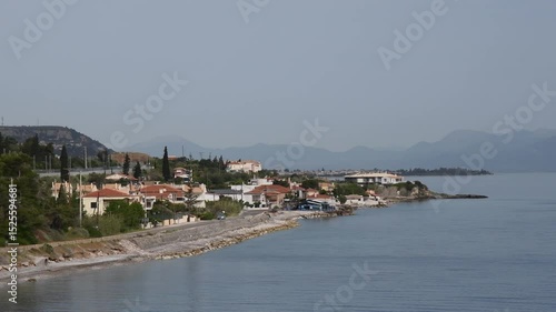 Explore Mavra Litharia Greece showcasing beautiful coast scenery with serene waters reflecting charming villages and mountains under bright sky. Pan camera moves to terracotta tiles rooftop
