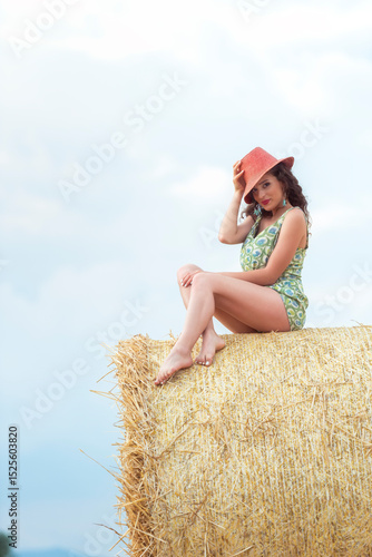 Woman sitting on hay bale with calm expression under the afternoon sun