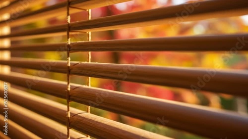 Close up of wooden blinds with blurred autumn leaves visible through the window in soft sunlight
