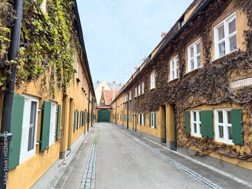 Historic alley in the Fuggerei, the world’s oldest social housing complex, located in Augsburg, Germany, with colorful facades and green shutters.
