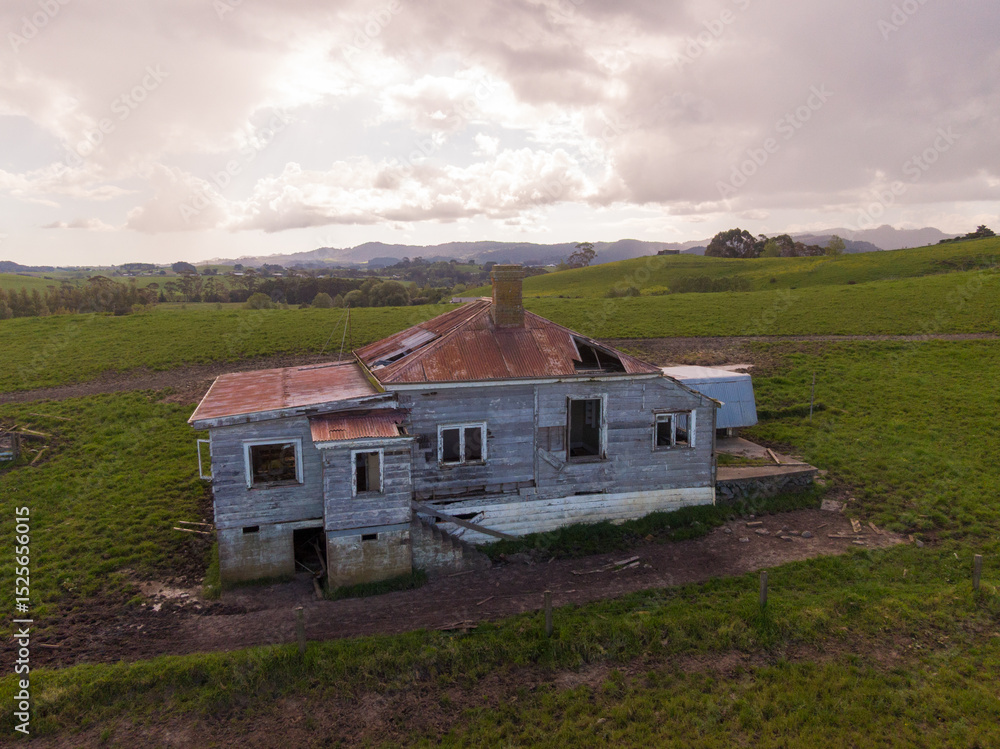 Obraz premium A decaying abandoned house with a rusty roof stands on a green rural hillside, a symbol of neglect and the passage of time. Matakana, Warkworth, Auckland, New Zealand