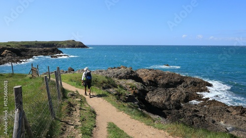 Paysage de côte sauvage à Saint-Malo en Bretagne, avec un randonneur marchant seul sur le sentier du littoral, au bord de la mer, sur le chemin de grande randonnée GR34 (France)