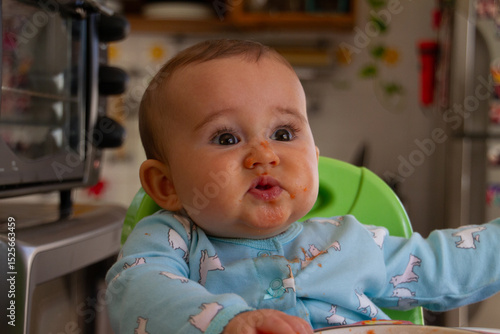 A lovely smiling baby sitting in a high chair, with a food-covered face, symbolizing the joy and mischief of mealtime moments.