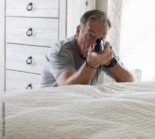 Tableau sur toile A senior citizen is protecting himself with a shotgun from an intruder in his be