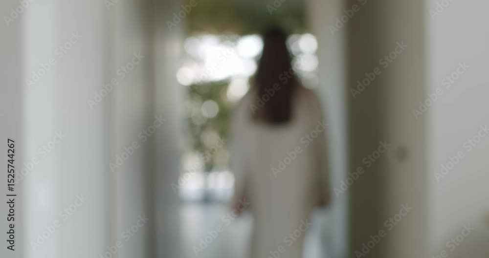 A woman in a white robe walks down a hallway towards a bright, plant-filled room. The video evokes feelings of peace, tranquility, and relaxation, perfect for lifestyle or wellness content.