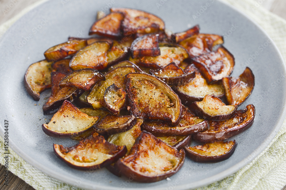 Fried quarter slices of eggplant or aubergine seasoned with salt and black pepper, served on blue plate (Selective Focus, Focus in the middle of the image) Fried quarter slices of eggplant or aubergine seasoned with salt and black pepper, served on blue plate (Selective Focus, Focus in the middle of the image)