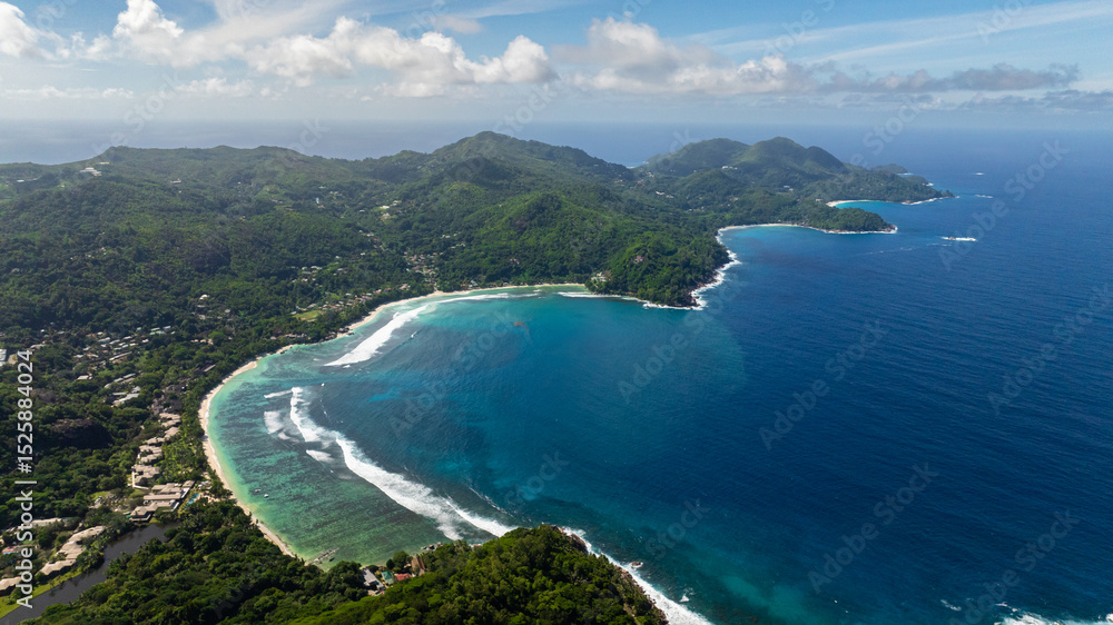 Obraz premium Clear turquoise waters flowing into a white sandy bay surrounded by lush greenery. Seychelles, Mahe.