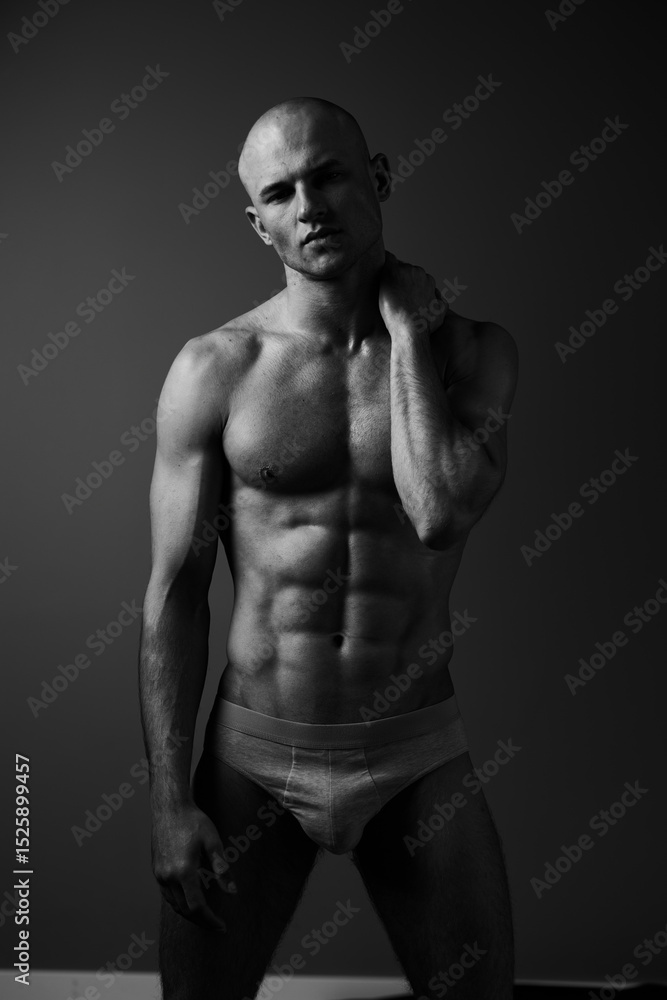 Fototapeta premium Athletic man posing confidently against a simple backdrop, showcasing a strong physique in a black and white composition, capturing strength and determination.