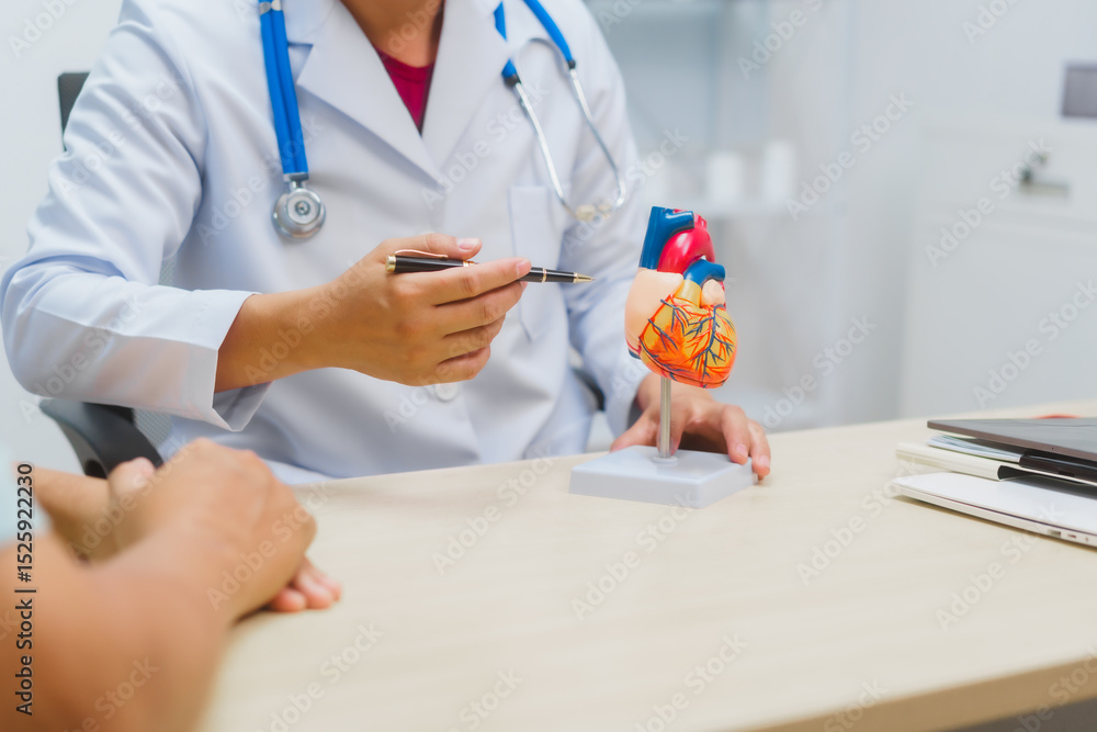 Asian male doctor specializing in cardiology explains heart disease to a patient using a heart model. He provides expert advice, discusses symptoms, risk factors, and treatment in a modern clinic. Asian male doctor specializing in cardiology explains heart disease to a patient using a heart model. He provides expert advice, discusses symptoms, risk factors, and treatment in a modern clinic.