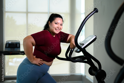 Portrait of young Asian overweight women exercising on elliptical trainer in the gym. Weight loss workout, healthy lifestyle concept.