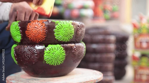 A skilled labourer or laborer paints a clay pot using vibrant colors and a sponge, showcasing traditional craftsmanship and artistic technique in a hands-on pottery decoration process. 4k Video 50 fps