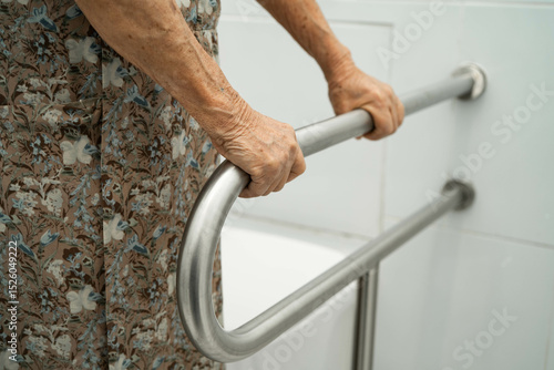 Asian elderly woman patient use toilet support rail in bathroom.