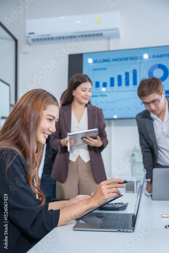 Group of business partners gathered around open laptop discussing company development strategies in modern office.