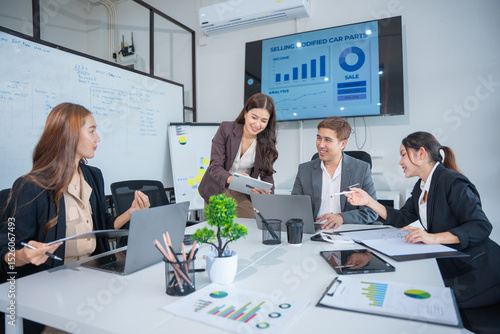 Group of business partners gathered around open laptop discussing company development strategies in modern office.
