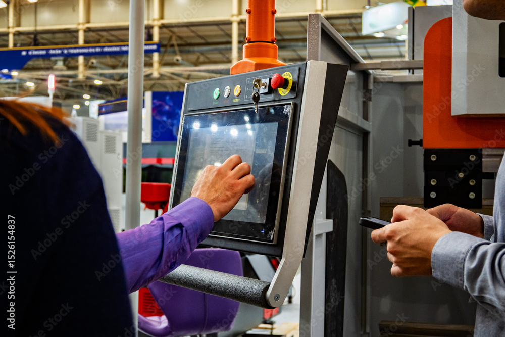 Fototapeta premium Industrial worker operating CNC machine control panel with touchscreen interface at manufacturing exhibition. Modern automated equipment with digital display and control buttons.