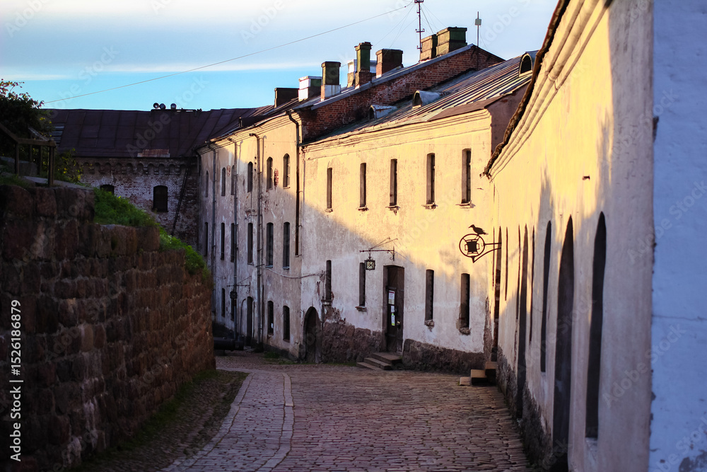 Fototapeta premium Sunset view of a street near Vyborg Castle in Russia, with old buildings and stone walls. Concept of medieval European architecture, historic towns, and atmospheric heritage streets