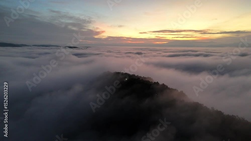 Serene sunrise over a misty mountain peak with clouds rolling across the horizon.