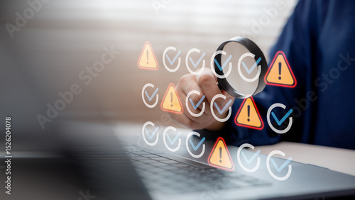 Hand using magnifying glass to inspect warning and check icons on laptop screen, representing system monitoring, debugging, error detection, and cybersecurity analysis.