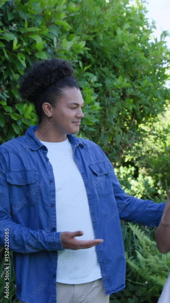 Vertical video: Diverse couple hugging then sitting in garden after woman holding rose, copy space Vertical video: Diverse couple hugging then sitting in garden after woman holding rose, copy space