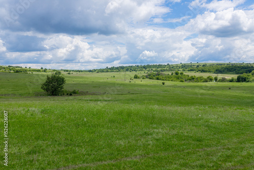 Tableau sur toile Wide lush green field stretches toward low hills