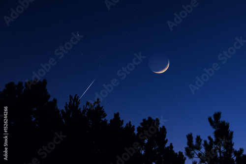 Countryside silhouettes under the stars, meteor trail and crescent Moon.