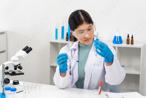 Canvastavla Asian female teenager wearing lab coat and blue gloves analyzing liquid in test tube while holding dropper