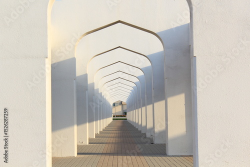 This image features a beautifully symmetrical architectural walkway composed of a series of white arches. The repeating geometric pattern creates a mesmerizing tunnel-like effect, leading the eye towa