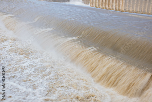 A turbulent, overflowing river in Florence, Italy. The water gushes over the rapids, creating foam and spray