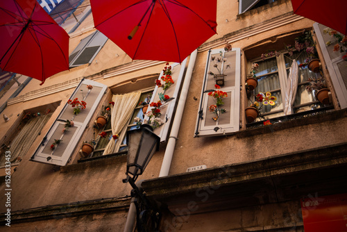 Fototapeta Naklejka Na Ścianę i Meble -  Beautifully decorated window of an old house. Window with open shutters and beautiful decor among red umbrellas decorating the street of an old town