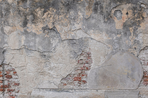 Old shabby stone wall with cracked plaster. The plaster has fallen off and exposed stones and brick. Texture of an old stone wall