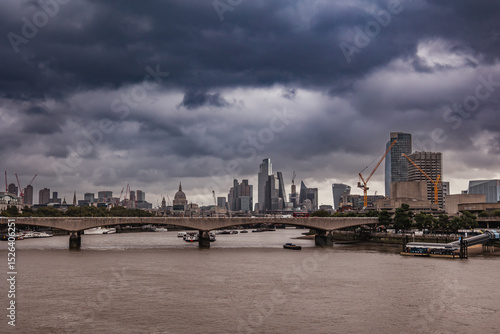 view from river thames of London Skyline with a bridge under a dark storm cloud