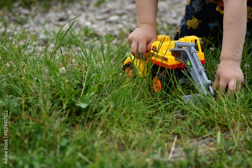 Wallpaper Mural Young boy plays with yellow toy truck close up on grass. Candid outdoor moment showing creativity and exploration in nature. No face anonymous. Torontodigital.ca