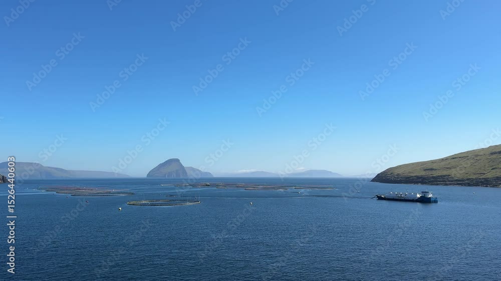 Sustainable salmon aquaculture facilities off the coast of Suðuroy, Faroe Islands, with Lítla Dímun island in the distance under clear blue skies. Sustainable salmon aquaculture facilities off the coast of Suðuroy, Faroe Islands, with Lítla Dímun island in the distance under clear blue skies.