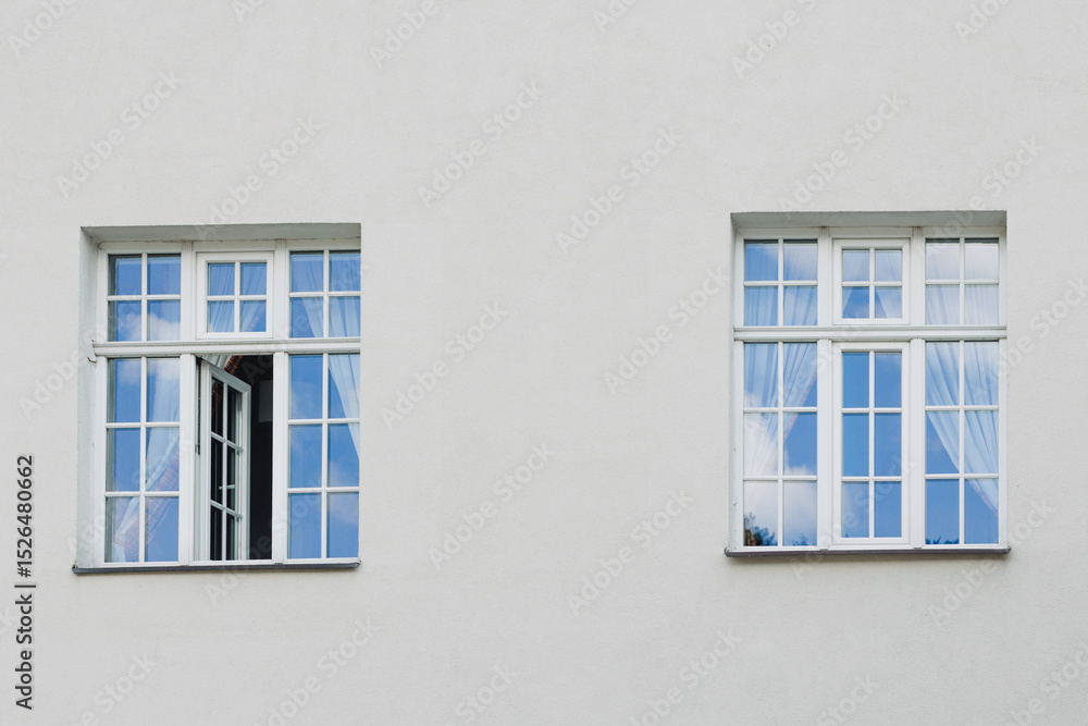 Fototapeta premium Windows with muntins reflecting blue sky on bright building facade, architectural detail showing symmetry, light, and classic window design elements