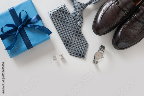 Happy Fathers Day greeting card with gift box. Set of classic mens clothes - brown shoes, wrist watch, necktie and blue gift on gray background. Men's accessories set. Top view. Copy space.