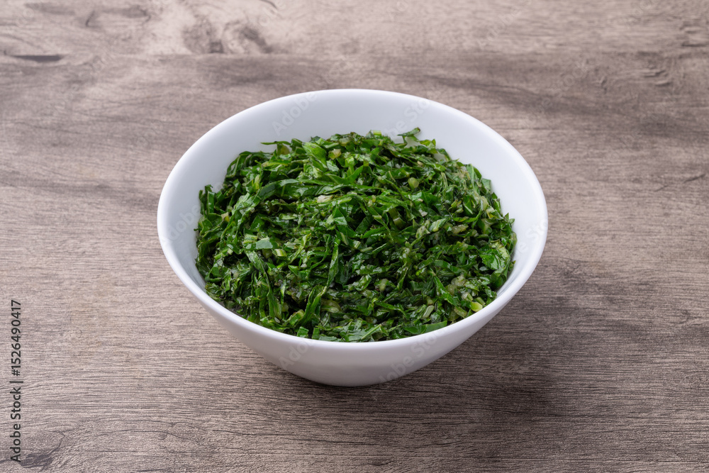 Cooked kale strips, typical brazilian feijoada sidedish in a bowl over wooden table Cooked kale strips, typical brazilian feijoada sidedish in a bowl over wooden table