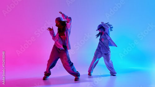 Fotografía Two confident teen girls grooving in motion, dressed in baggy denim outfits under bright gradient lights in studio fog